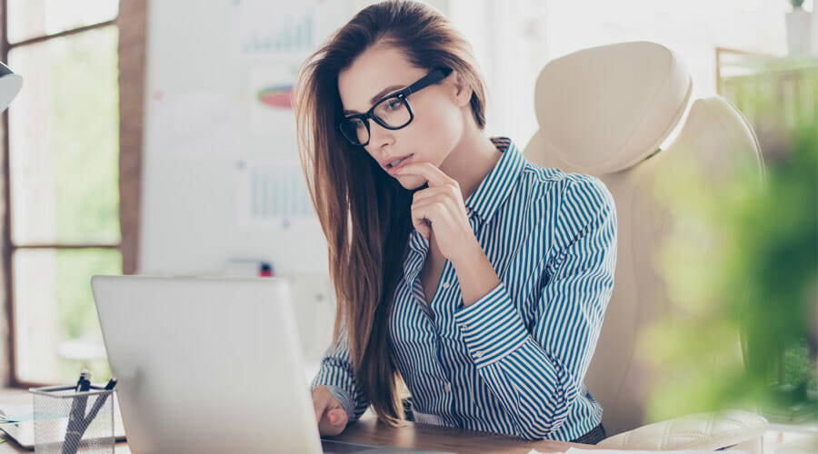 A smartly dressed woman with glasses using a laptop