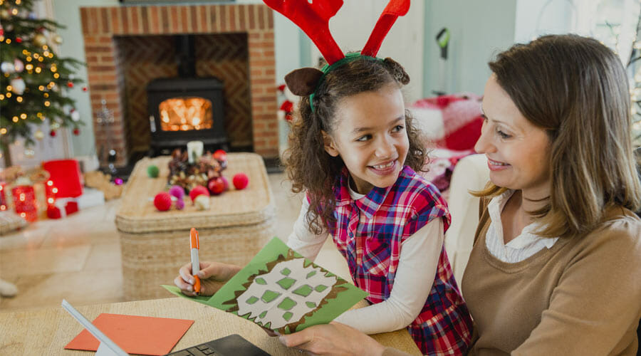 a child sat on their mother's lap whilst making a christmas card