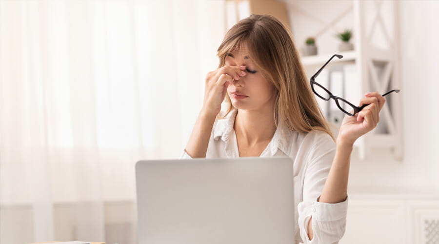 a woman rubbing the bridge of her nose whilst taking a break from her laptop
