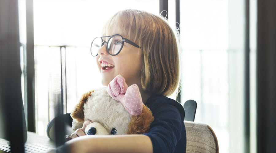 A little girl with glasses smiling and hugging her stuffed toy dog