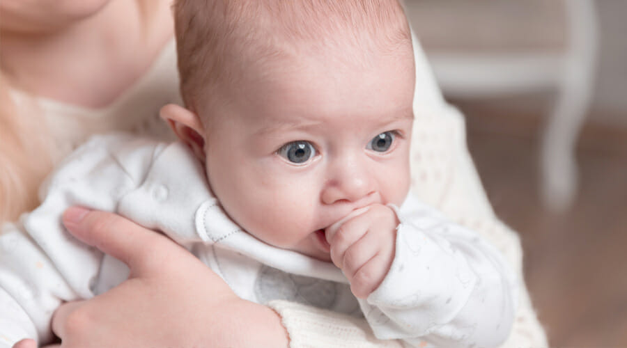 a parent holding their baby whilst the baby sucks on their thumb