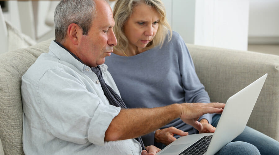 an elderly couple sat on the sofa whilst using a laptop