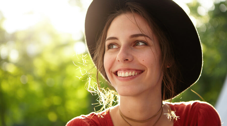 a woman in a hat smiling with the sun behind her