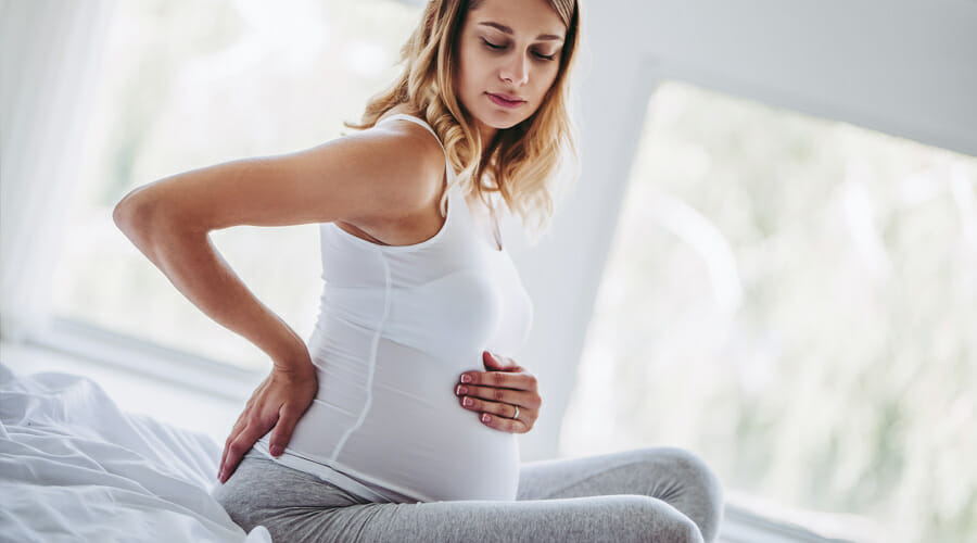 A pregnant woman holding her back and baby bump