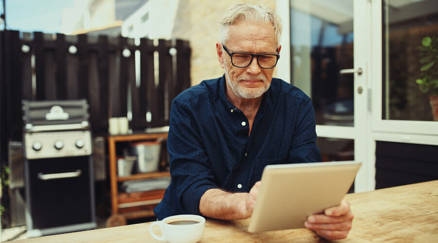 Blog-cataracts-three-symptoms-show-need-see-eye-surgeon-Samer-Hamada-eye-clinic-london an elderly man enjoying a coffee in his garden whilst using his tablet