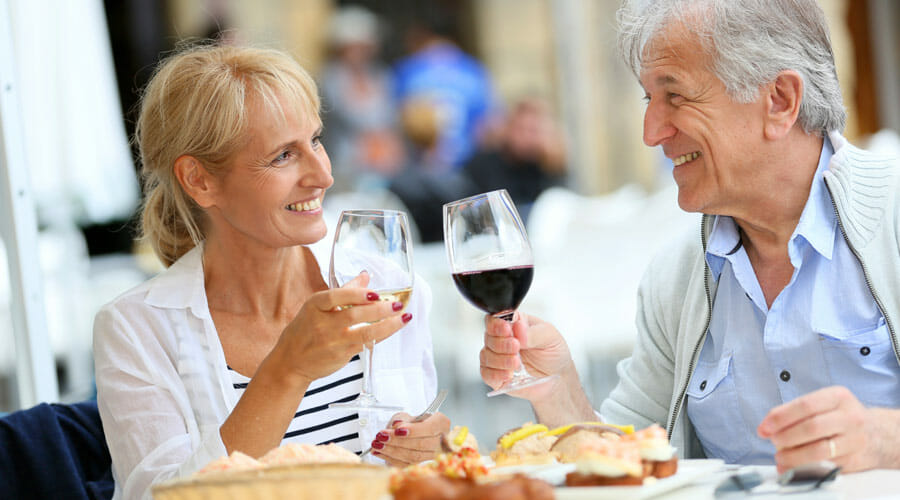 an elderly couple eating food and drinking wine at a restaurant