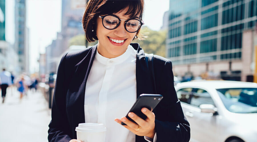 a woman holding a cup of coffee whilst smiling and looking at her phone