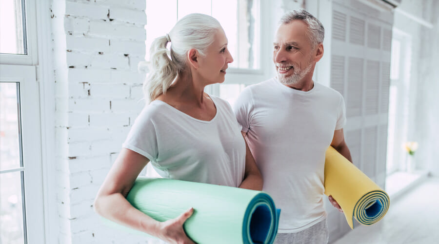 An older couple looking at each other and smiling whilst holding yoga mats