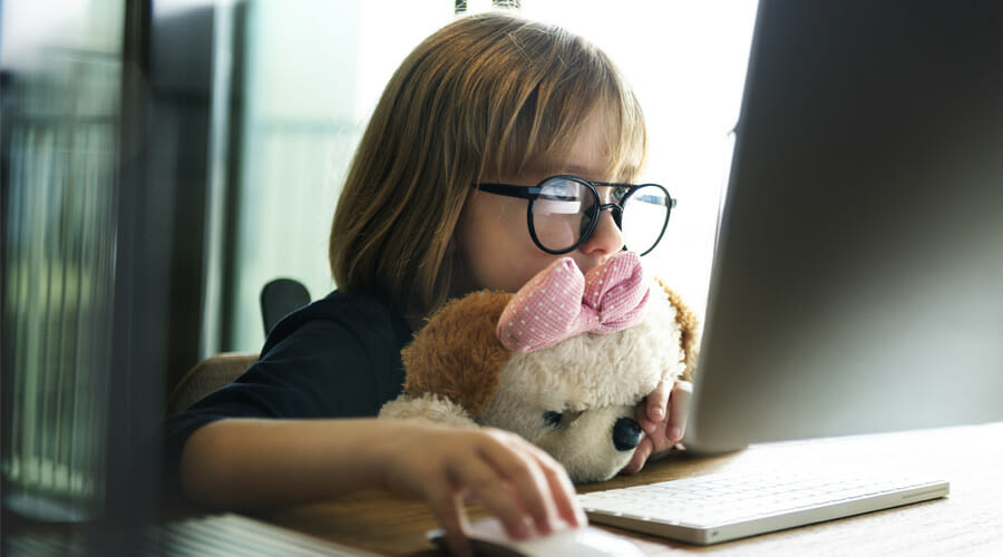 Blog-eye-specialist-parents-not-leave-childs-squint-untreated-Samer-Hamada-eye-clinic-london A child with glasses sat at a desk whilst leaning on her stuffed animal. She staring intently at an Apple computer.