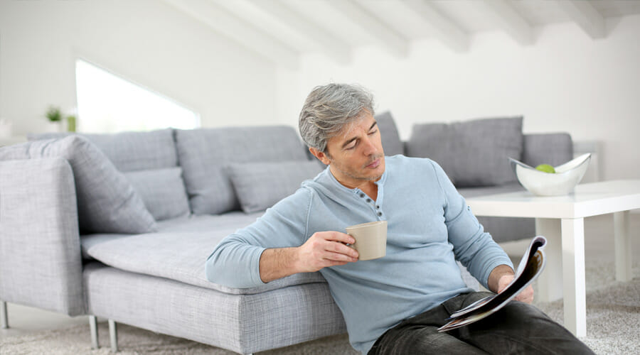 a man sitting on the floor in his living room whilst drinking coffee and reading a magazine