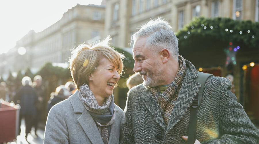 an older couple walking through a christmas market, laughing and smiling at one another