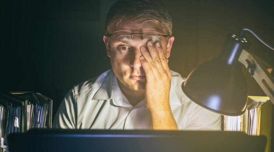 A man rubbing his eyes whilst working at his desk