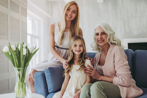 Step-3-children-samer-hamada-eye-clinic-london A photo of two women and a girl sitting on a sofa whilst smiling into the camera. The little girl is sat in the middle, the older woman is sat to the left of the girl and the younger woman is sat on the arm of the sofa in the background.