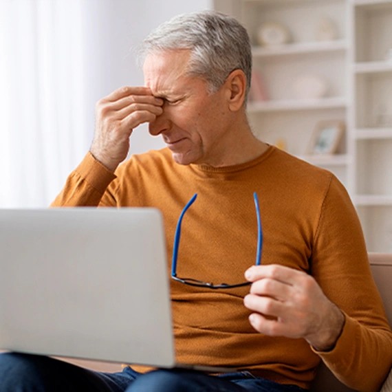 Man with tired, irritated eyes at a laptop