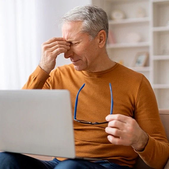 Man with tired, irritated eyes at a laptop